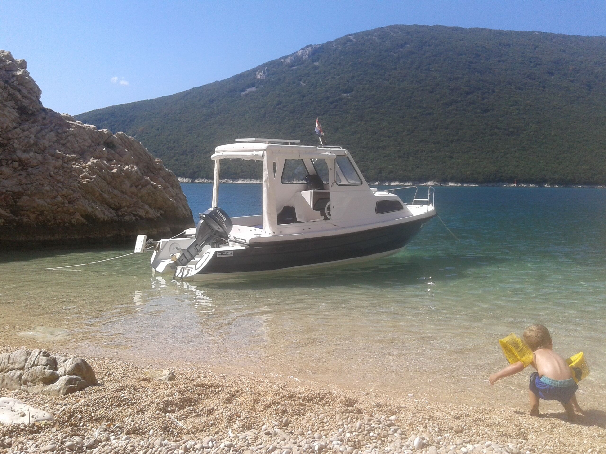 A boat docked at a rocky shore with clear water and a mountain in the background.