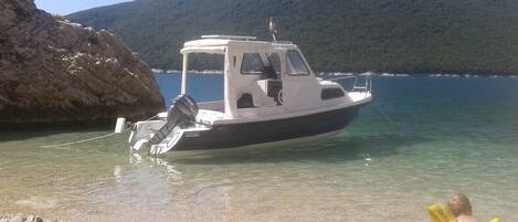 A boat docked at a rocky shore with clear water and a mountain in the background.
