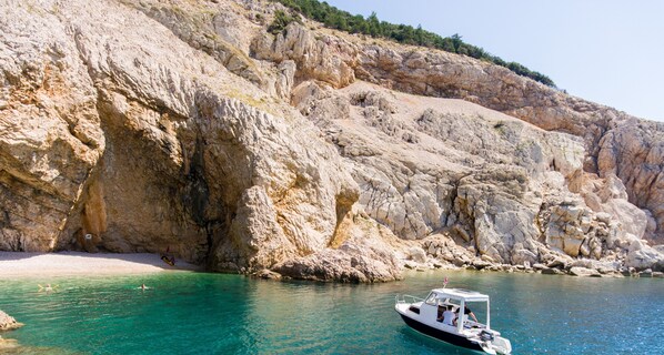 A boat on a turquoise sea with a rocky cliff in the background.