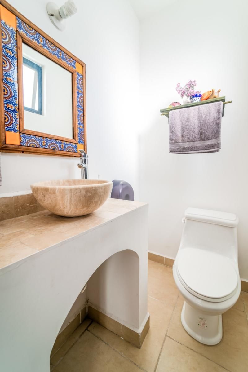 A bathroom with a large basin, a toilet, a towel rack with a towel, and a mirror with a decorative frame.