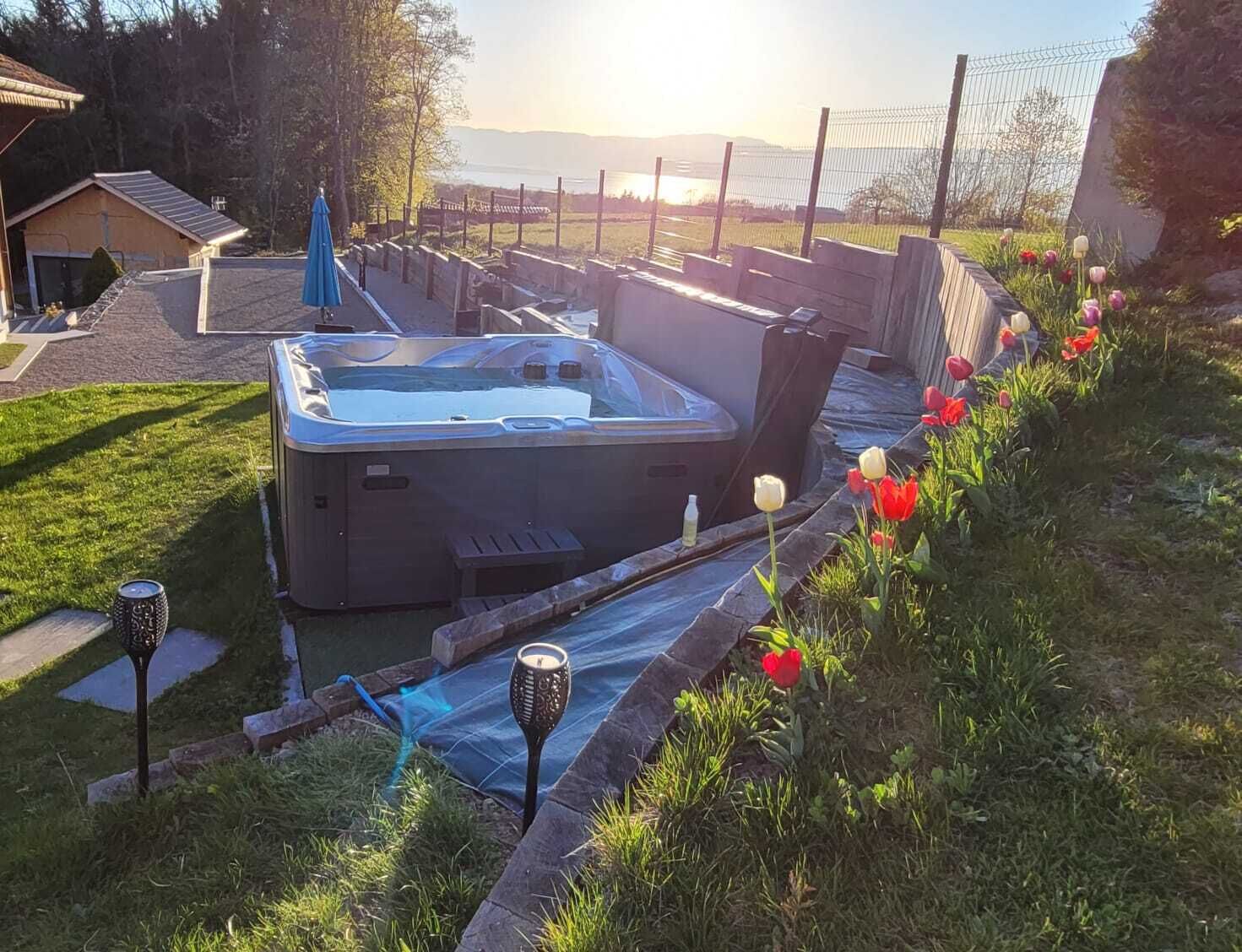 A hot tub in a garden with a view of the sunset and mountains.