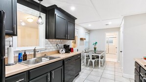 A modern kitchen with black cabinets, a dishwasher, a sink, and a dining area with a table and chairs. - Stylish, Cute & Homey Livonia Getaway (Livonia)