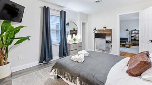 A modern bedroom with a bed, a TV, a plant, and a bathroom visible through an open door. - Stylish, Cute & Homey Livonia Getaway (Livonia)