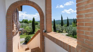 Une vue depuis un balcon aux murs de briques et à l’arche, donnant sur un paysage rural avec des arbres et un ciel dégagé.