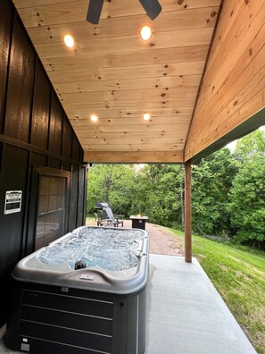 A hot tub under a wooden ceiling with a patio area, a grill, and a sign indicating a hot tub rental.