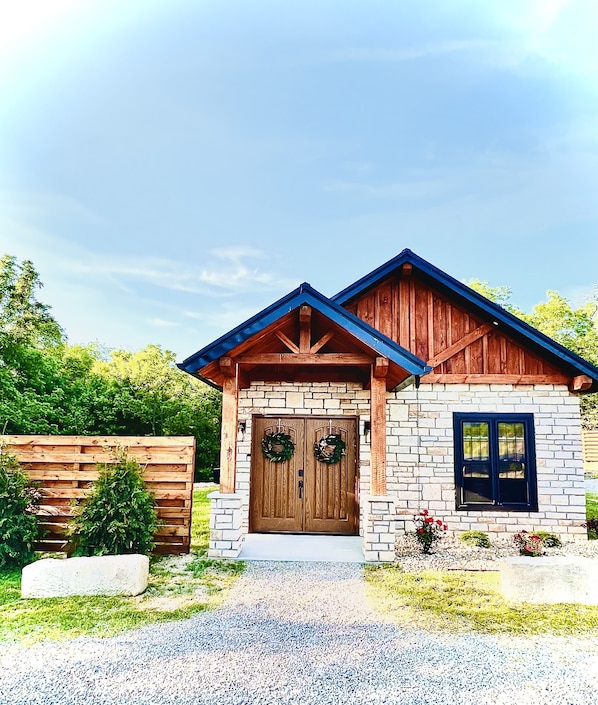 A two-story house with a stone facade, a wooden front porch, and a blue roof.