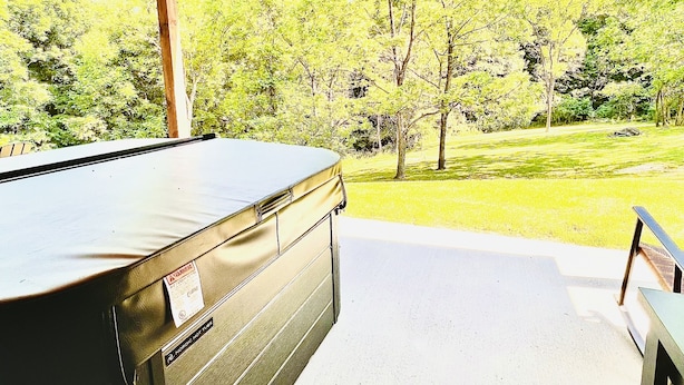 An outdoor hot tub area with a wooden deck and a view of a green landscape. - LUXURY COUPLES CABIN! Caveside Cabins (Creola)