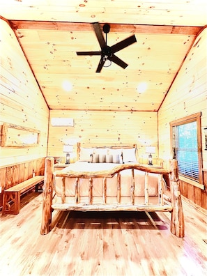 A log cabin bedroom with a wooden bed, a ceiling fan, and a window with blinds.