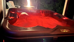 A hot tub with a fire feature, surrounded by a wooden deck and trees. - LUXURY COUPLES CABIN! Caveside Cabins (Creola)