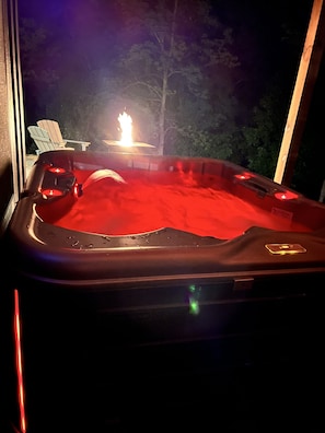 A hot tub with a red interior, surrounded by a wooden deck and two Adirondack chairs.