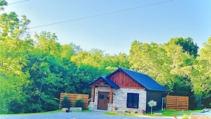 A small stone building with a red roof, surrounded by lush green trees. - LUXURY COUPLES CABIN! Caveside Cabins (Creola)