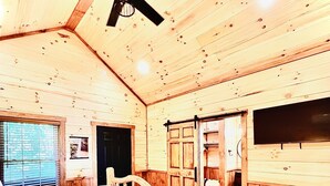A wooden cabin bedroom with a bed, a ceiling fan, and a large window. - LUXURY COUPLES CABIN! Caveside Cabins (Creola)