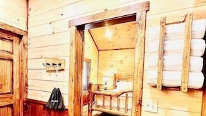 A wooden interior with a wooden bench, a table, and a hanging coat rack. - LUXURY COUPLES CABIN! Caveside Cabins (Creola)