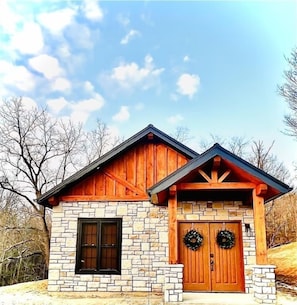A stone building with a wooden facade, a gabled roof, and a front door with two wreaths.
