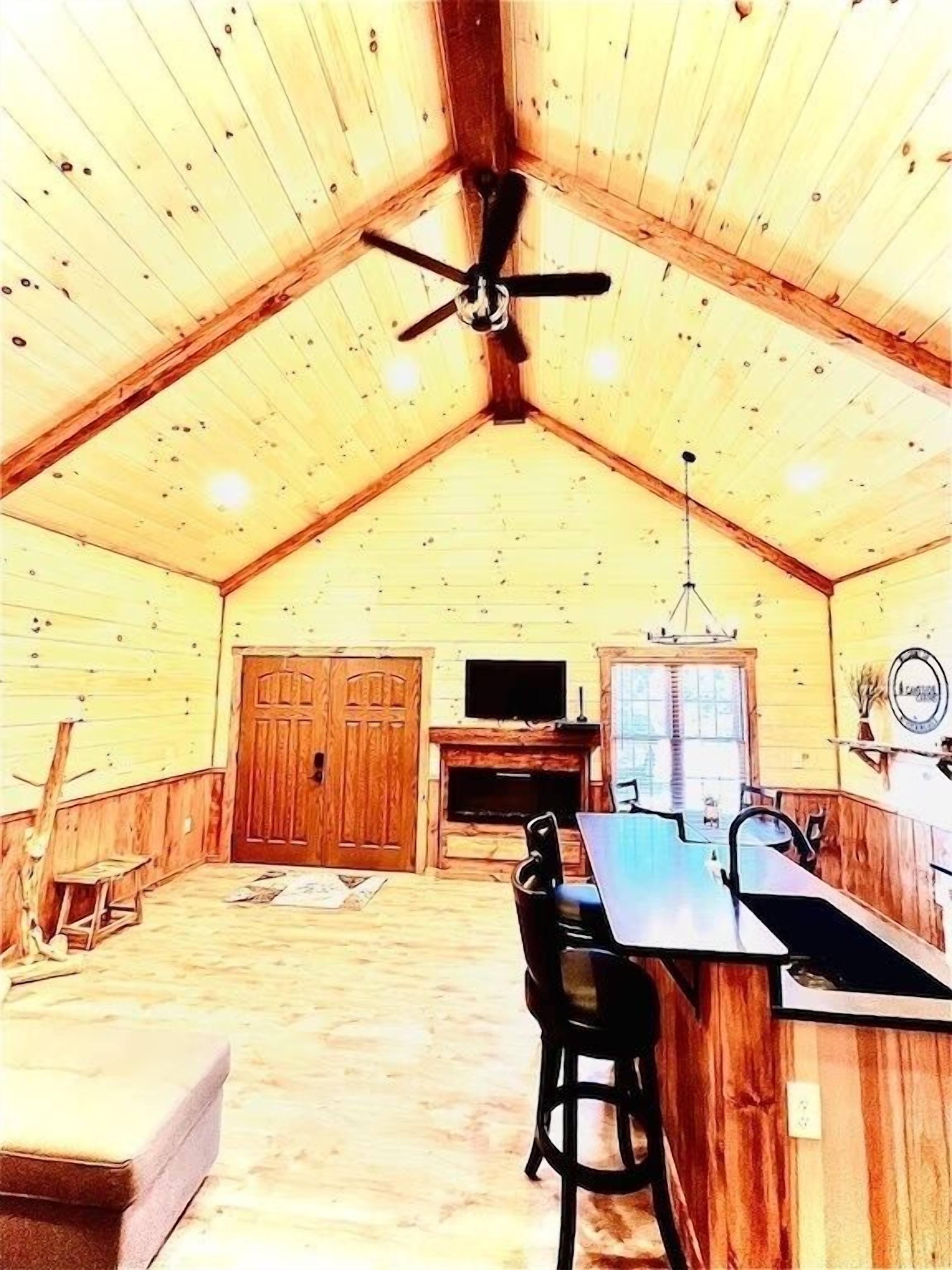 A rustic interior with a wooden ceiling, a ceiling fan, a bar area, and a fireplace.