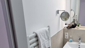 Een badkamer met een witte handdoek op een radiator, een wastafel, een spiegel en een prullenbak.