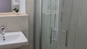 Een moderne badkamer met een douche met glazen wand, een witte wastafel en een spiegel boven de wastafel.