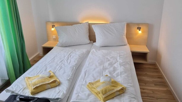 Een tweepersoonsbed met witte lakens en twee kussens, aan elke kant een nachtkastje en een wandlamp.