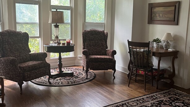 Uma sala de estar com dois poltronas, uma mesa redonda, uma mesinha de centro e um tapete estampado.