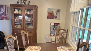 Uma mesa de jantar de madeira com quatro cadeiras, uma máquina de café, um armário com portas de vidro e um quadro na parede.