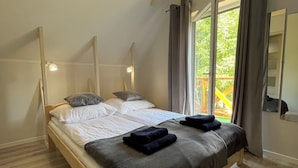 Ein Schlafzimmer mit einem hölzernen Bett, weißer Bettwäsche und Blick auf Grünfläche.
