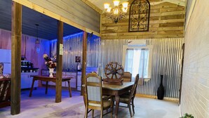 Un coin repas rustique avec une table et des chaises en bois, une roue décorative et une cuisine en arrière-plan.