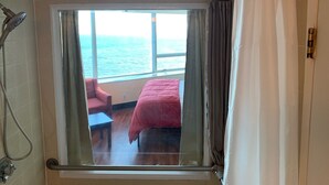 A room with a large window, a bed, a chair, and a shower.
