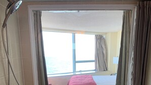 A bathroom with a large bathtub, a showerhead, and a window with curtains.