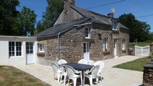 A stone house with a tiled patio, white chairs, and a table. - Country house with indoor pool, near Rochefort en terre; 2 stars. (Saint-Gravé)