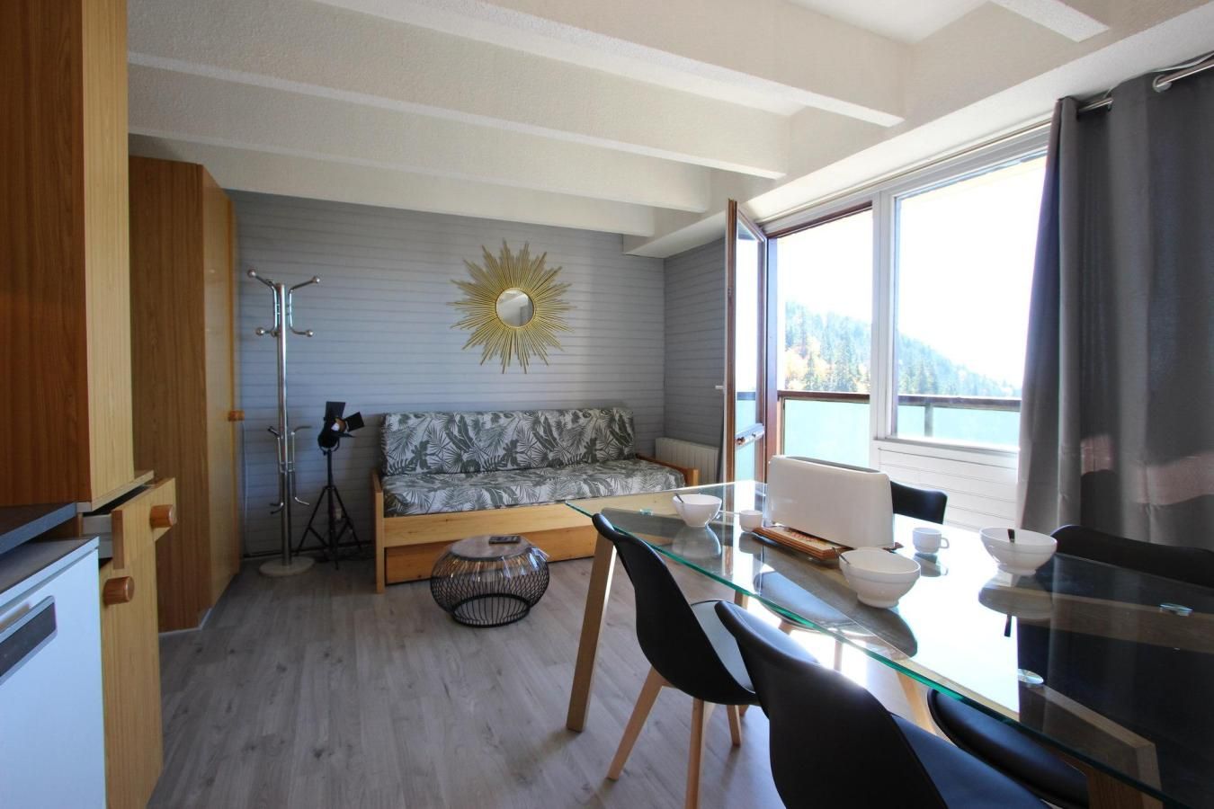 A compact living space with a sofa, a glass dining table, and a tripod stand.