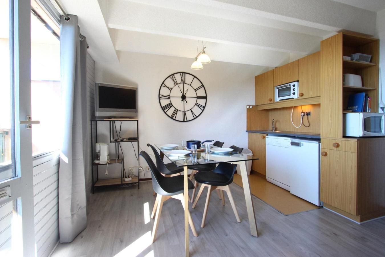 Une cuisine compacte avec un coin repas, une grande horloge murale et un four à micro-ondes.