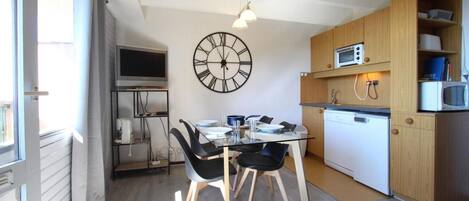 A compact kitchen with a dining area, a large wall clock, and a microwave.
