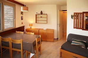 A dining area with a table and chairs, a wooden cabinet, a wall-mounted shelf with decorative items, and a sofa.