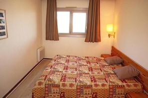 A bedroom with a bed, a window with curtains, a wall-mounted lamp, and a radiator.