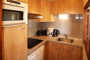 A compact kitchen with wooden cabinets, a built-in oven, a coffee maker, and a dishwasher.
