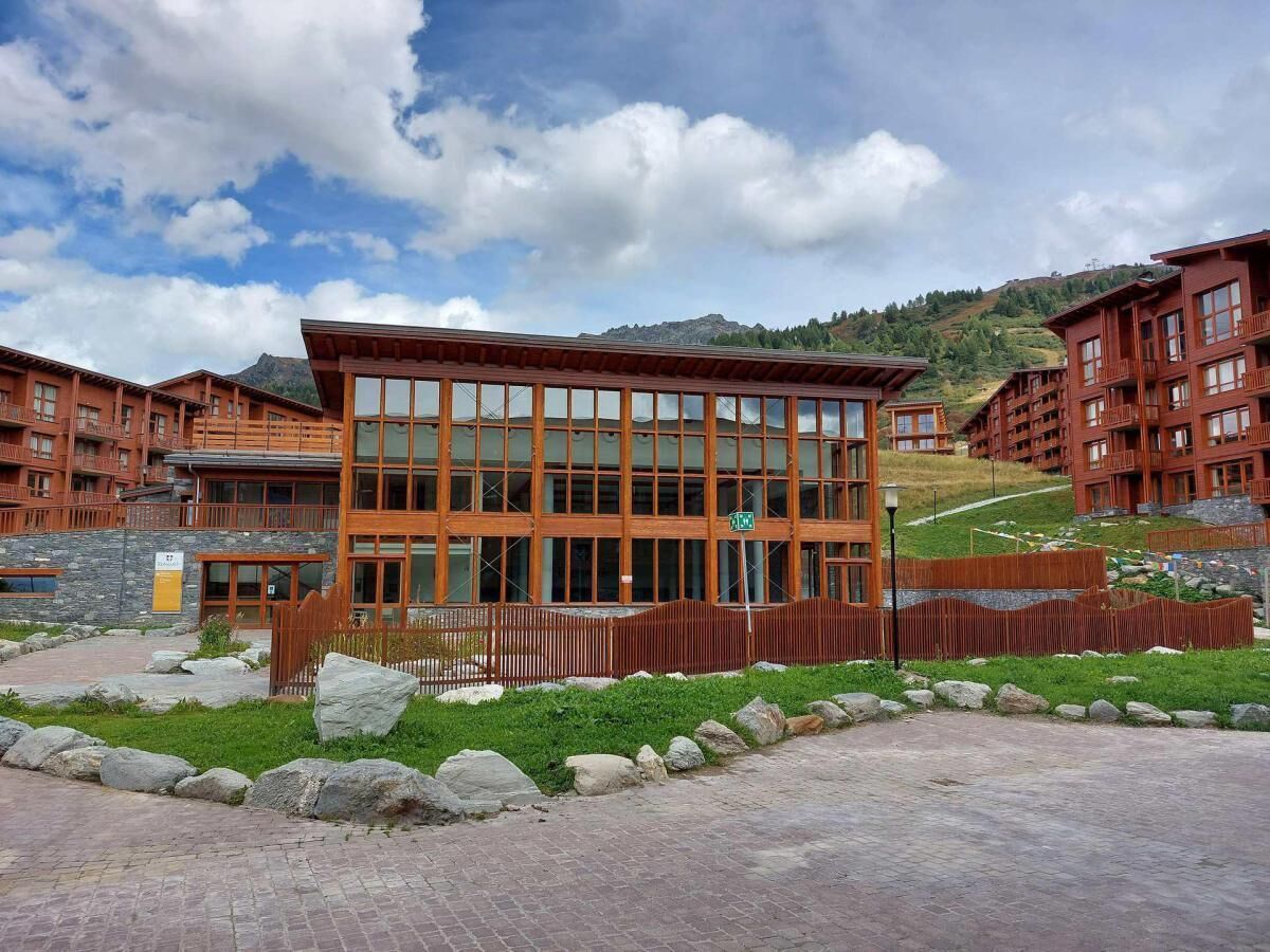 A modern building with large windows and a wooden facade, surrounded by a landscaped area with rocks and grass.