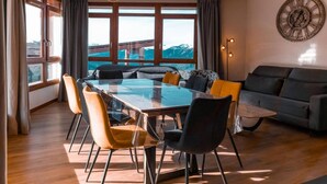 A modern living room with a glass dining table, comfortable seating, a sofa, and a large window offering a view of the outdoors. - Ski-in/ski-out & foot of the slopes, 2nd floor, view open, fitness, swimming pool, balcony (Les Arcs)