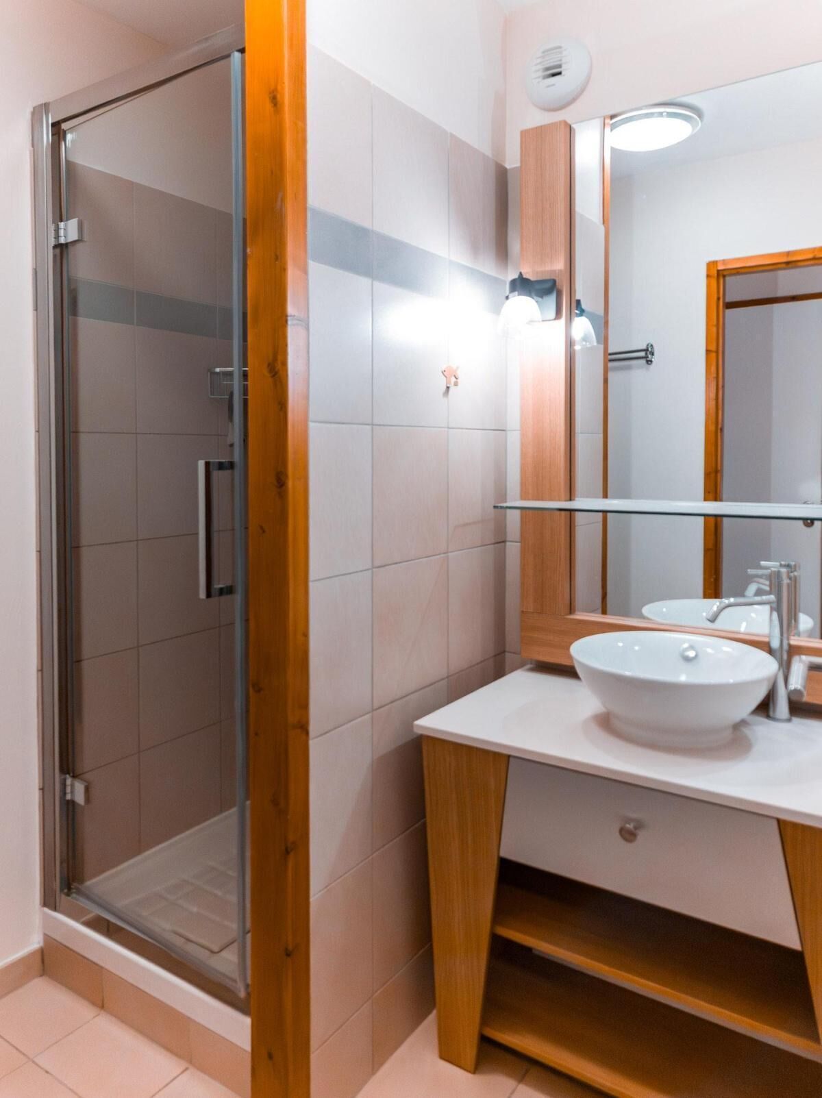 A modern bathroom with a glass shower enclosure, a white sink, and a wooden vanity.