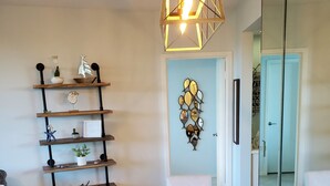 Een eethoek met een witte tafel, stoelen en een hanglamp. Er is een plank met decoratieve objecten en een kunstwerk aan de muur.