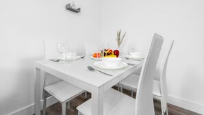 Une table de salle à manger blanche, avec des chaises, un panier de fruits et une petite plante.