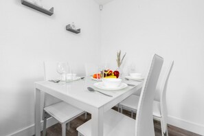 Ein weißer Esstisch mit Stühlen, einer Obstschale und einer kleinen Pflanze.