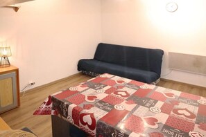 A small room with a bed covered in a patterned blanket, a blue sofa, a bedside lamp, and a wall clock.