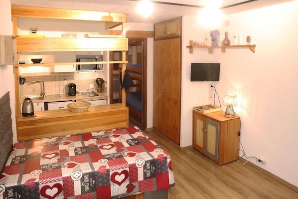 A compact room with a bunk bed, kitchenette, and a television mounted on the wall.