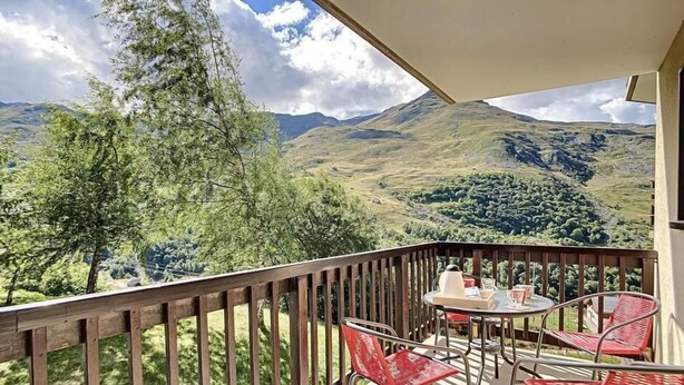 Een balkon met een houten hekwerk, een tafel met stoelen en uitzicht op een bergachtig landschap.