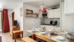 Een compacte keuken met witte kastjes, een magnetron en een koffiezetapparaat. Er staat een eettafel gedekt met borden, bestek en glazen.