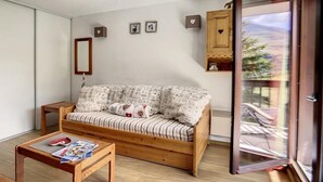 Een gezellige woonkamer met een houten bank, een klein houten tafeltje en een glazen deur die leidt naar een balkon.