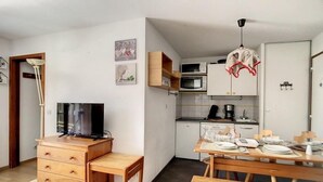 Een kleine leefruimte met een kitchenette, een eethoek en een televisie op een houten dressoir.