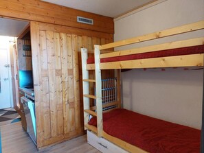 Una cama litera con colchón rojo, paredes de madera y una pequeña zona de kitchenette con un lavamanos y estufa.
