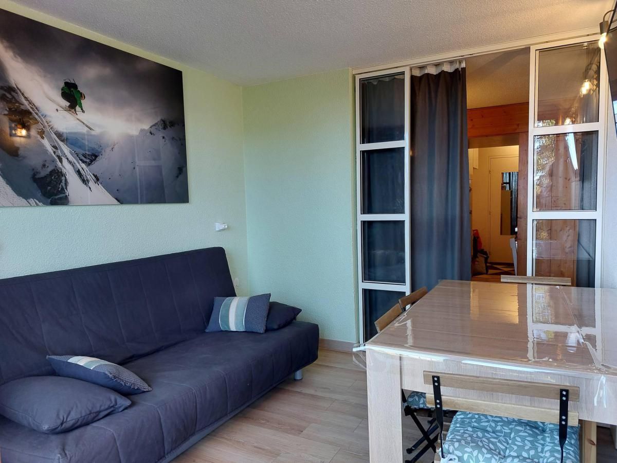 A room with a dark blue sofa, a glass-top table, and a painting of a skier on a mountain.