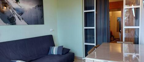 A room with a dark blue sofa, a glass-top table, and a painting of a skier on a mountain.